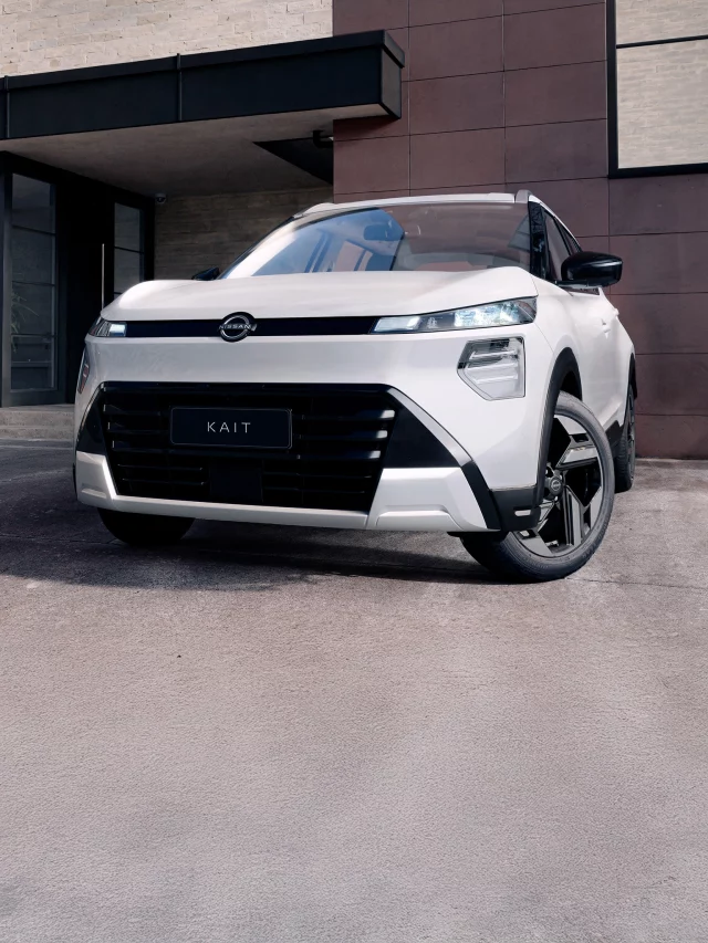 Vista frontal de um SUV Nissan KAIT branco estacionado em frente a uma fachada de prédio moderna em tons de marrom e preto, com iluminação natural.