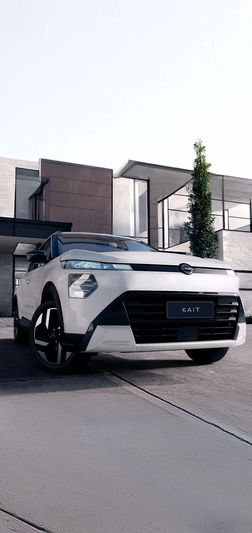 Vista frontal de baixo de um SUV Nissan KAIT branco estacionado em frente a uma residência moderna com diferentes texturas. O design frontal angular e as luzes são destacados.