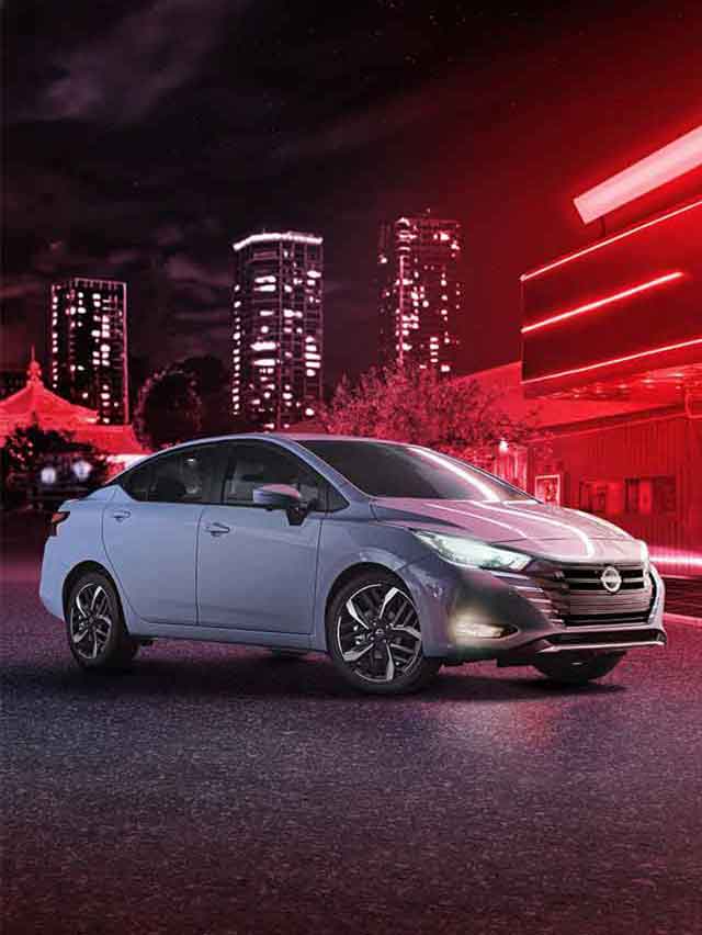 Carro Nissan Versa em uma rua iluminada por luzes vermelhas, com skyline ao fundo e duas pessoas caminhando.