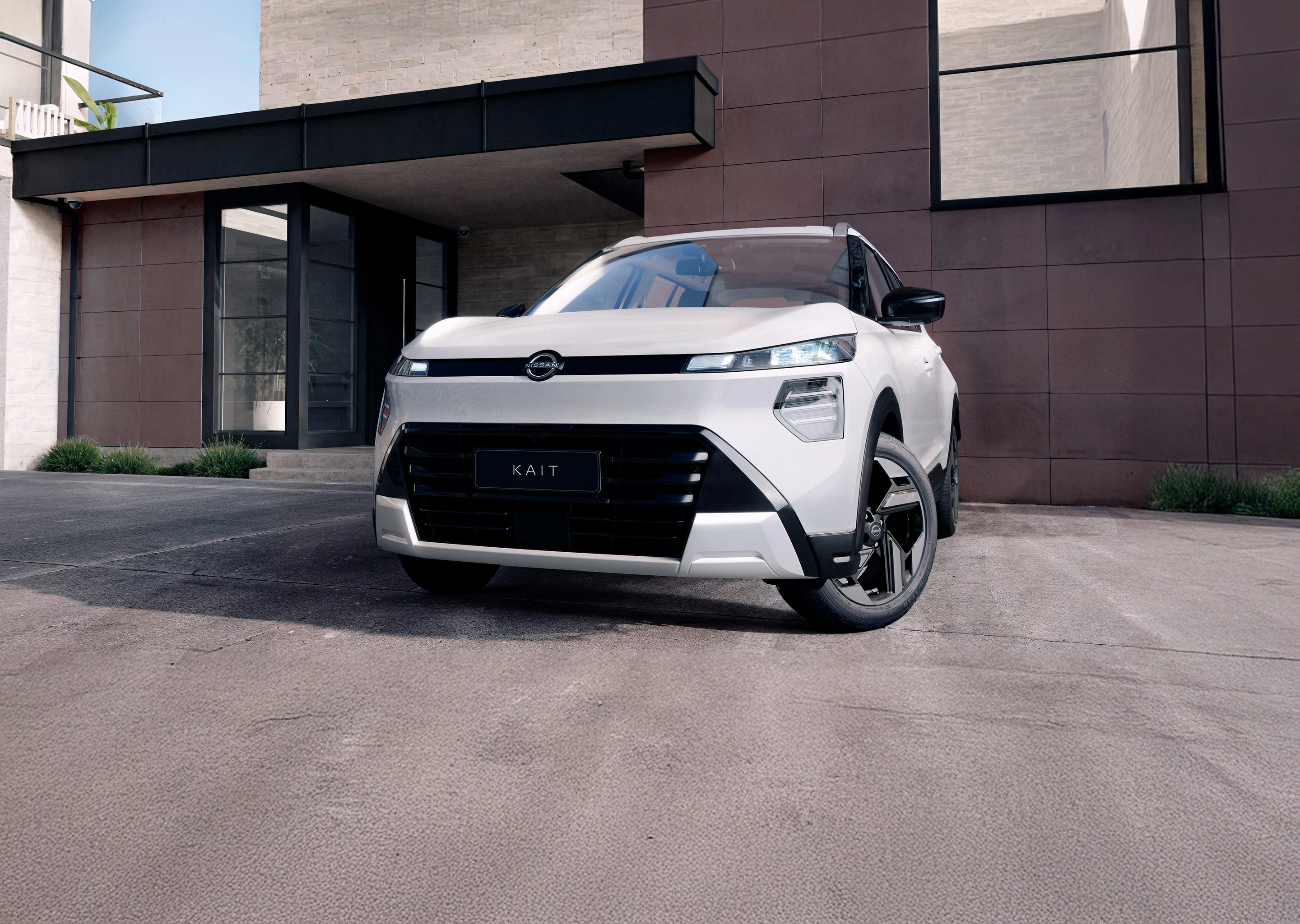 Vista frontal de um SUV Nissan KAIT branco estacionado em frente a uma fachada de prédio moderna em tons de marrom e preto, com iluminação natural.